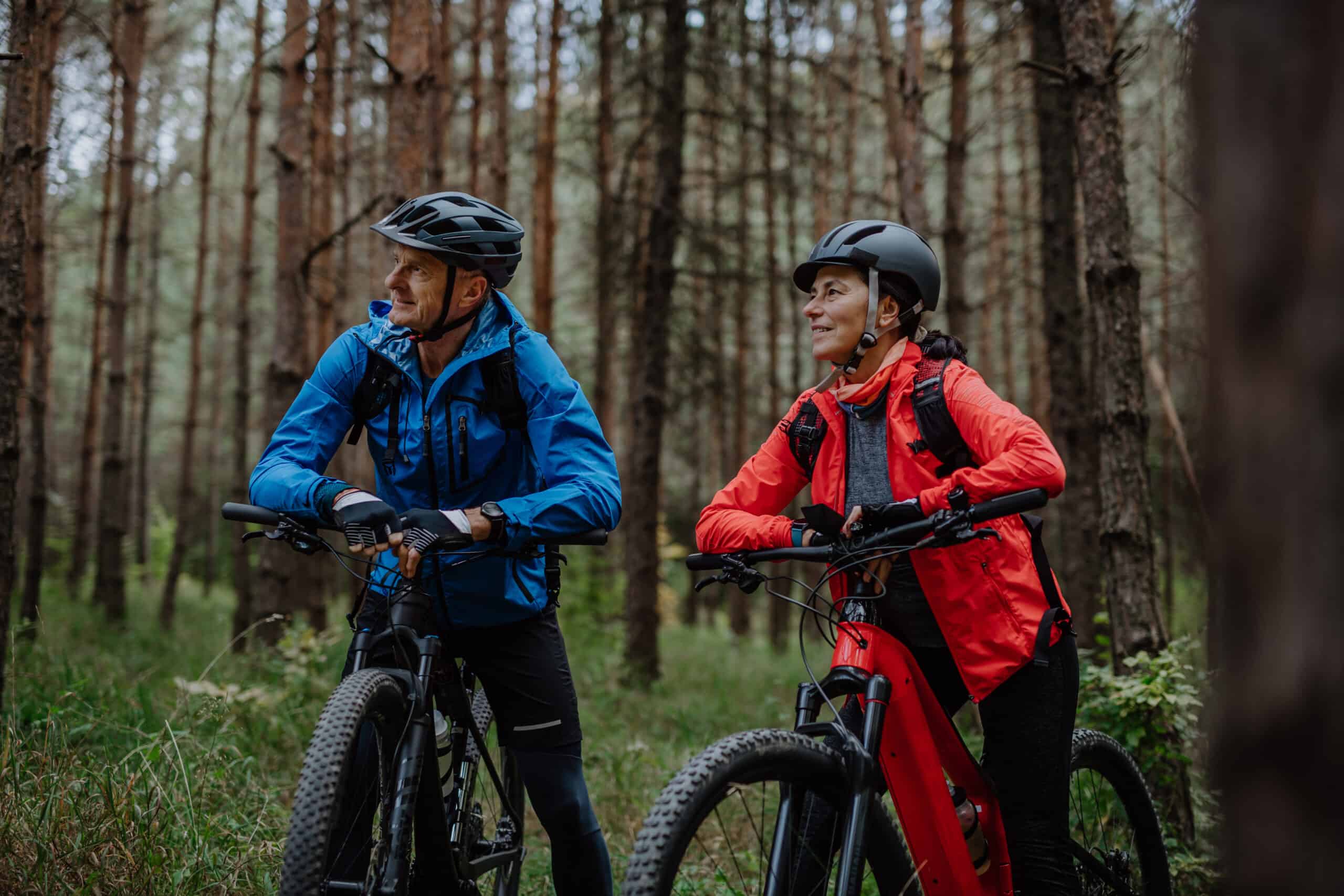 Senior couple bikers with e-bikes admiring nature outdoors in forest in autumn day. | Harmony Javorník