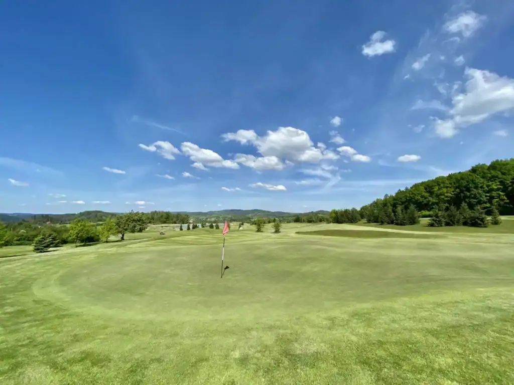 Golfové hřiště s modrou oblohou a zeleným trávníkem, ideální pro sportovní aktivity.