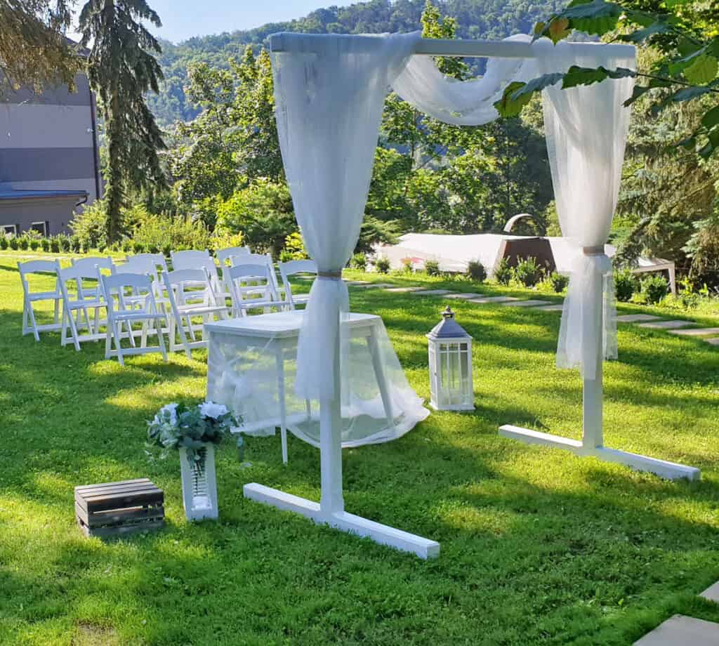 Svatební obřadní místo na zahradě s bílým baldachýnem a židlemi.
